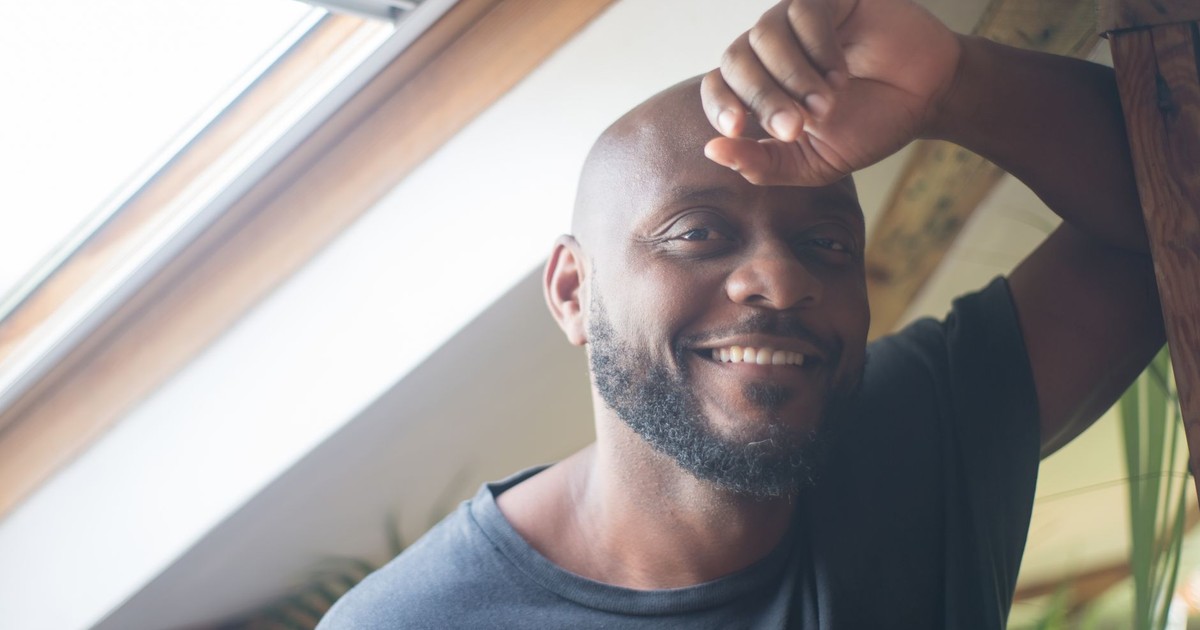 Portrait of a smiling man relaxing by a skylight, enjoying natural light indoors.
