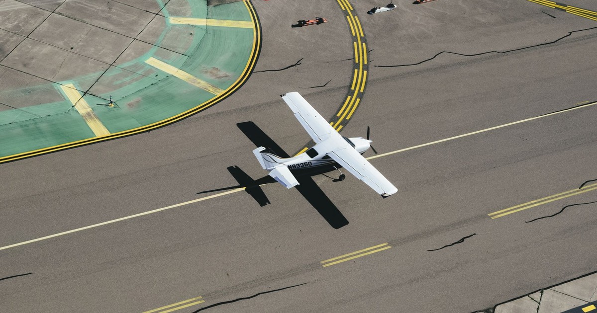From above of small biplane landing on runway with cracks and yellow markings on summer sunny day
