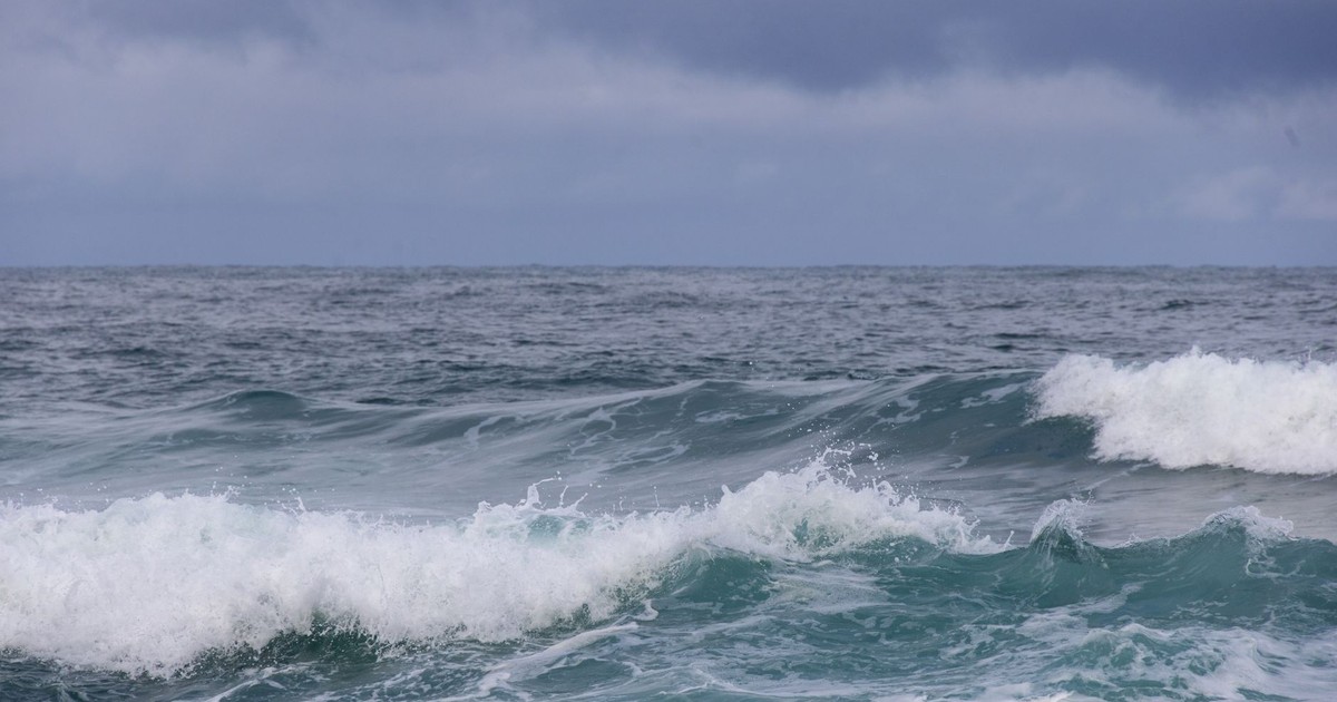 Powerful ocean waves crash beneath a moody, overcast sky, showcasing nature's raw energy.