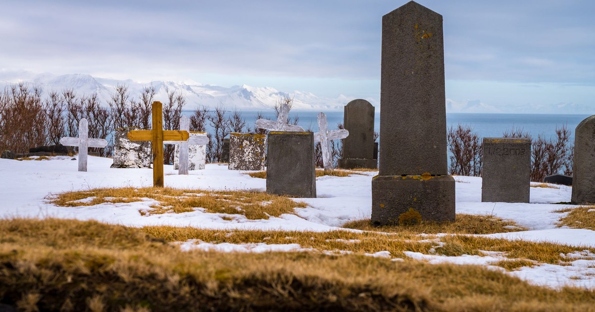 Serene winter cemetery view with tombstones against an ocean backdrop and snowy foreground.