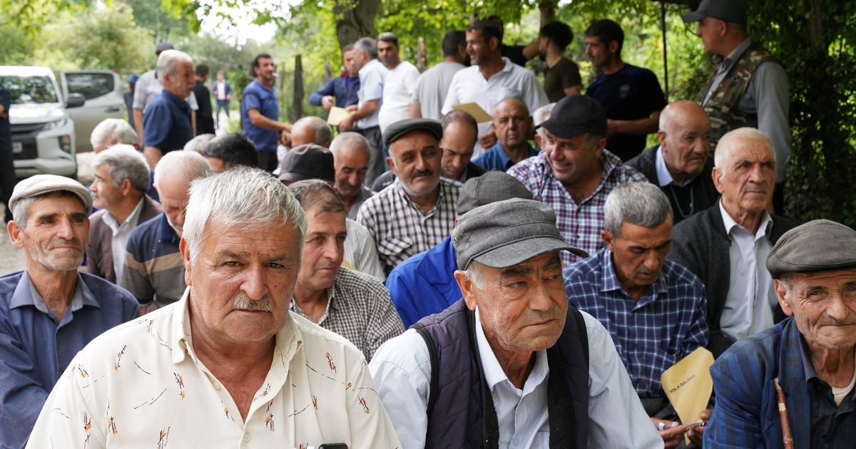 Senior men gathered outdoors, engaging in social interaction under trees.