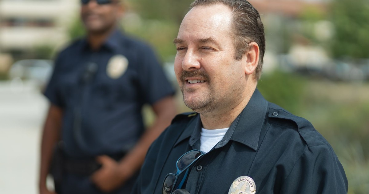 Two police officers smiling outdoors in uniform, representing community service.