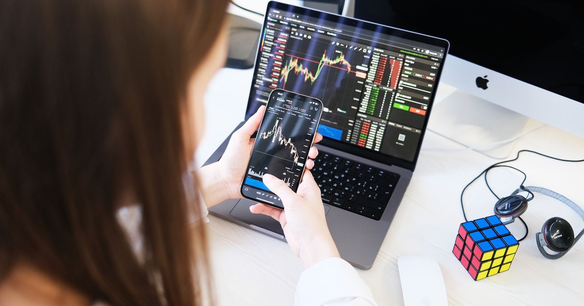 A woman trading cryptocurrency with charts on a smartphone and laptop, showcasing digital finance technology.