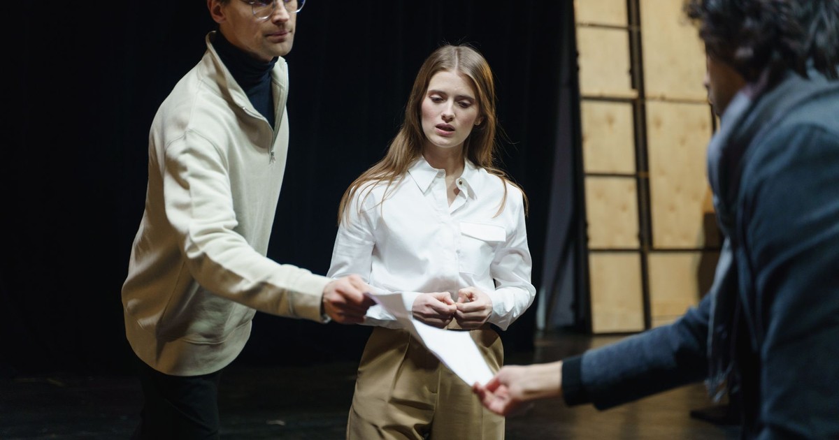 Actors engage in a rehearsal, exchanging scripts on stage, embodying theatrical drama and emotion.