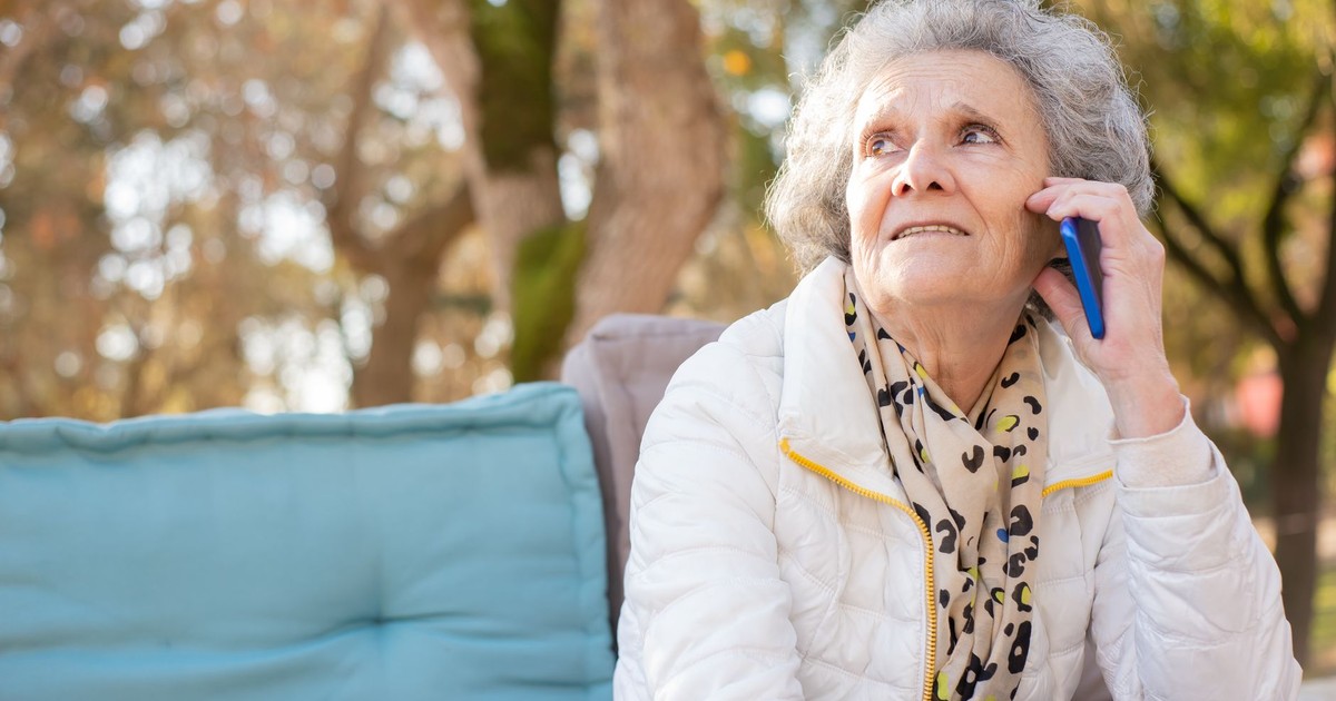 Senior woman in white jacket having a phone conversation in an outdoor park setting.
