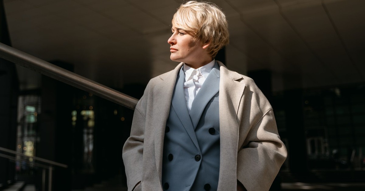 Stylish businesswoman with short hair in a coat, standing confidently outdoors in urban environment.