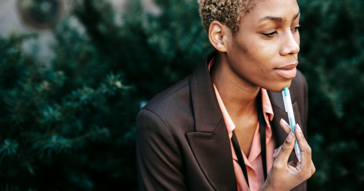 High angle of crop African American female entrepreneur in formal suit touching chin with pen while thinking about business