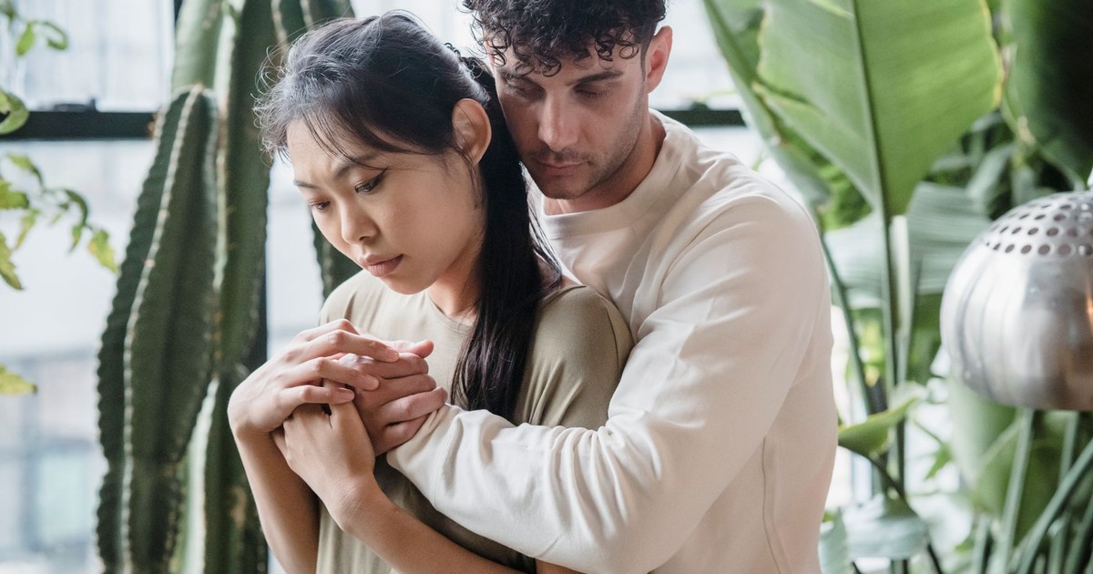 A couple shares an intimate back hug surrounded by large indoor plants.