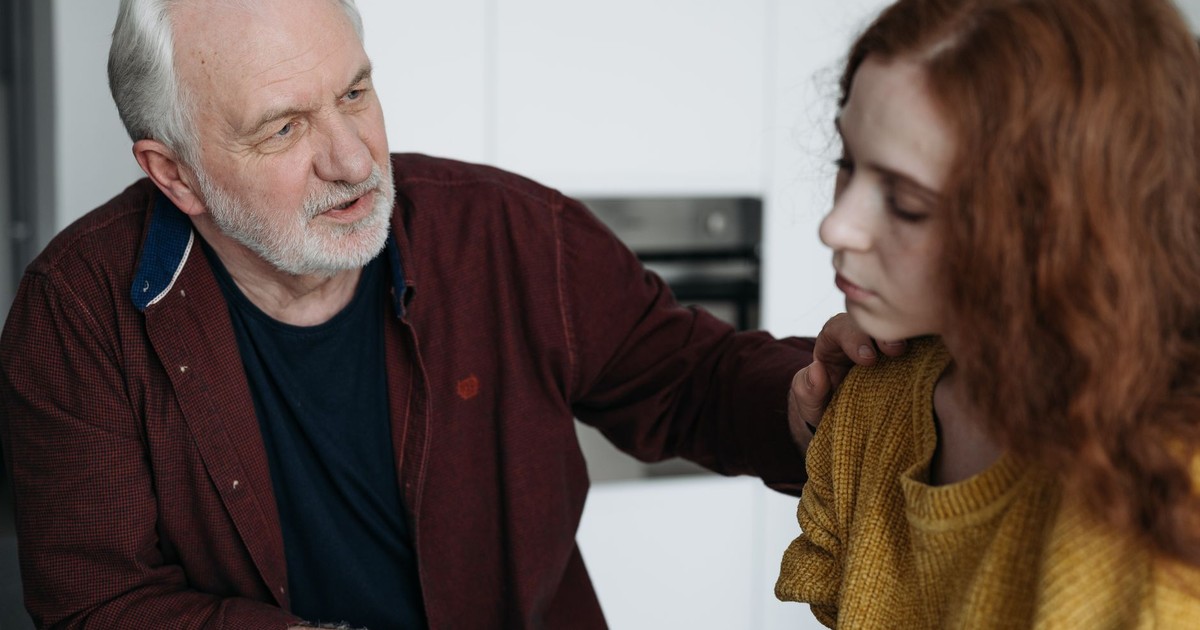 An elderly man consoles a young woman indoors, expressing empathy and understanding.