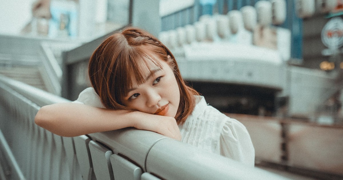 A woman with a stylish haircut leans on a metal railing in an urban setting.