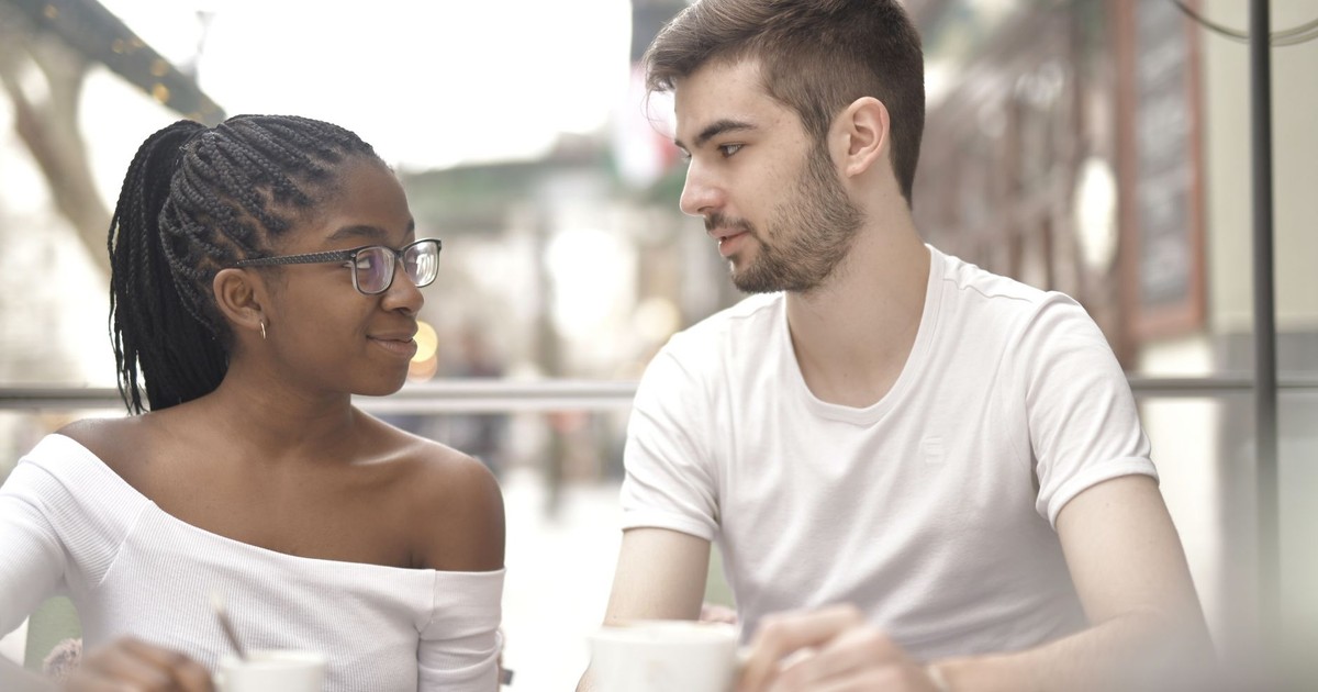 A multiracial couple enjoys coffee together in a bright café setting, sharing a warm moment.