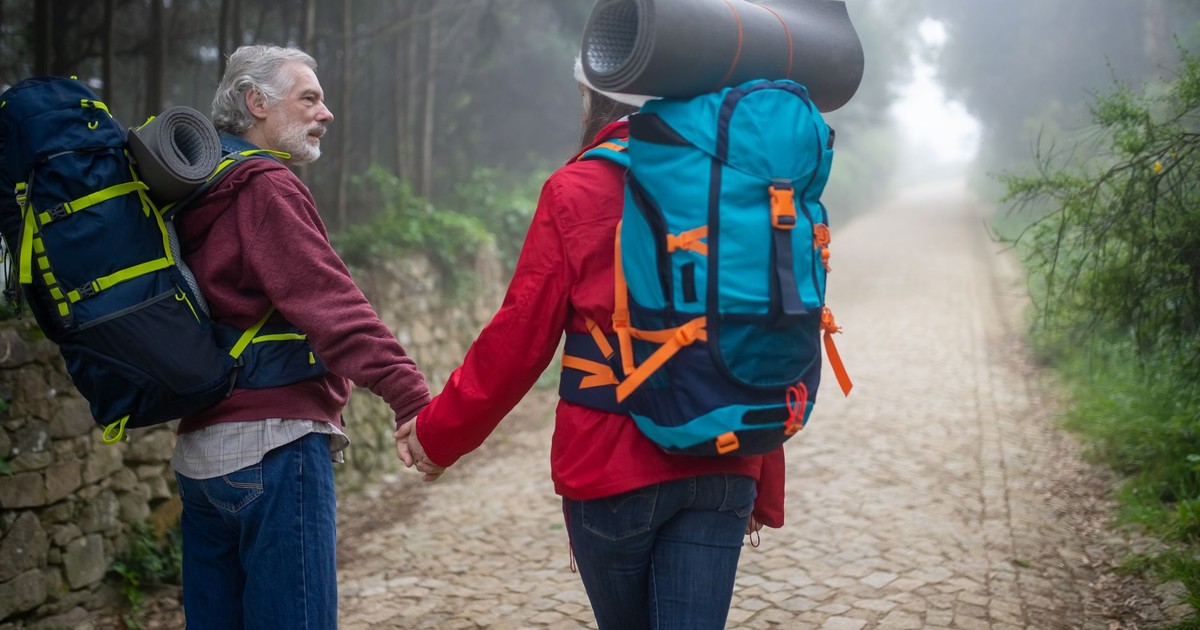 An elderly couple hiking hand in hand through a foggy path surrounded by nature in Portugal.