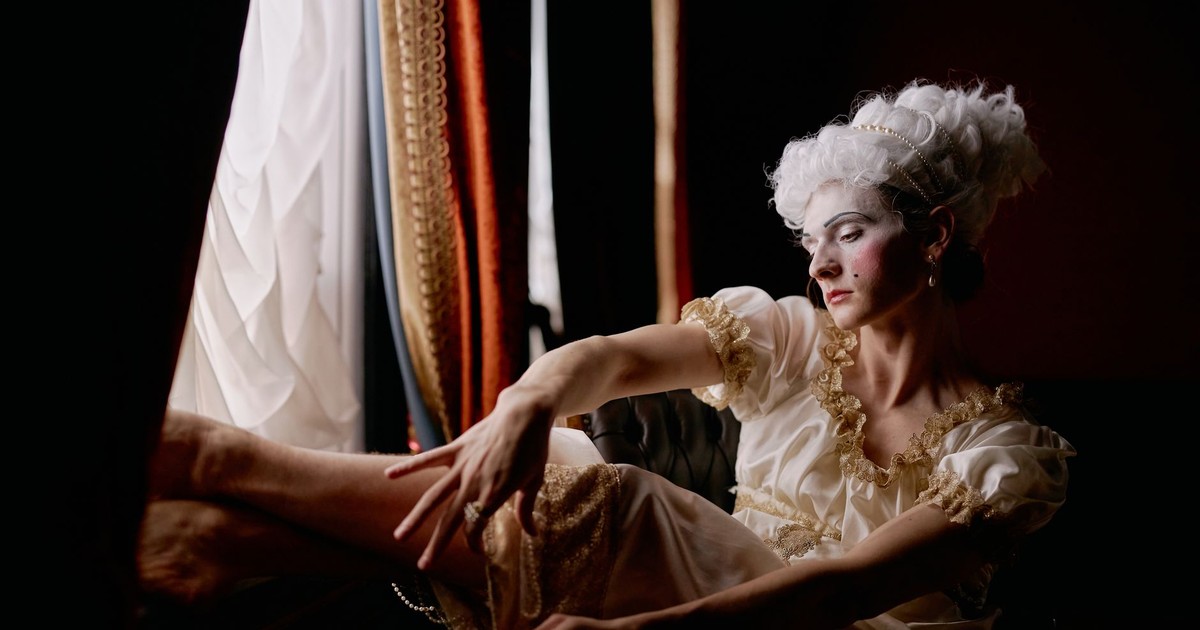 Dramatic portrait of a woman in historical costume by window, capturing elegant theatrical expression.