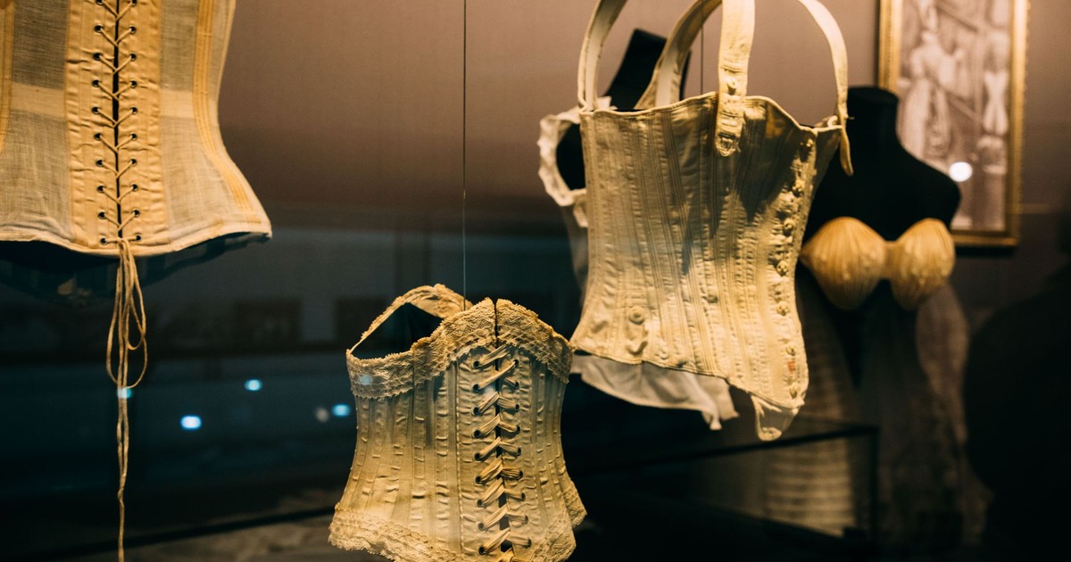 Showcase with collection of historical corsets with laces near picture on wall on exhibition