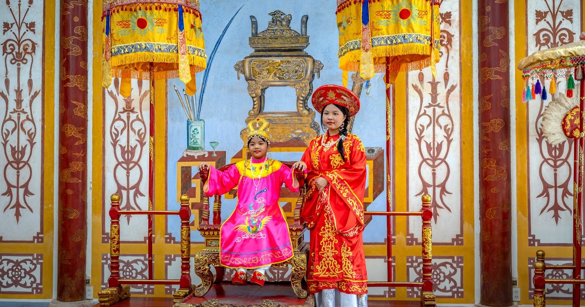 Two people in traditional Vietnamese royal attire inside a decorated room.