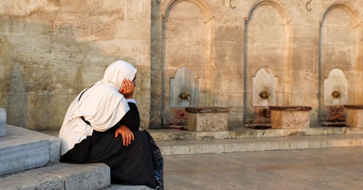 A woman sits in reflection by an ancient fountain at a mosque.