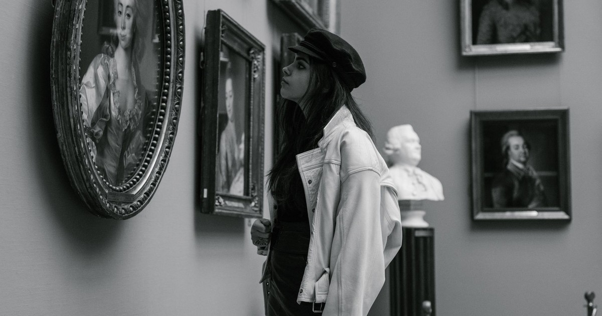 Black and white photo of a woman admiring paintings in a museum gallery.