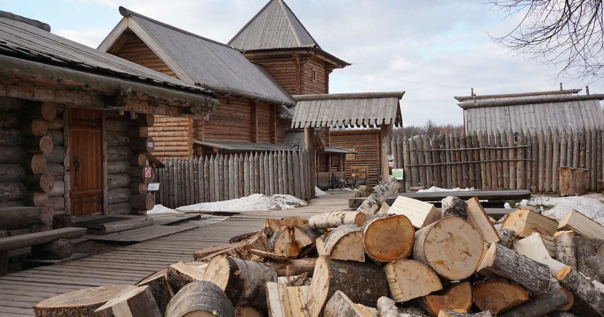 Chopped logs piled in front of traditional Russian wooden buildings, showcasing rustic architecture.