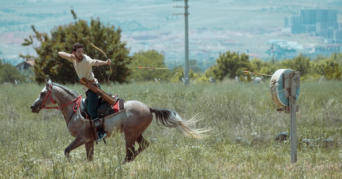 Dynamic scene of a mounted archer practicing in a field with a clear mountain backdrop in Konya, Türkiye. Captured outdoors in daylight.