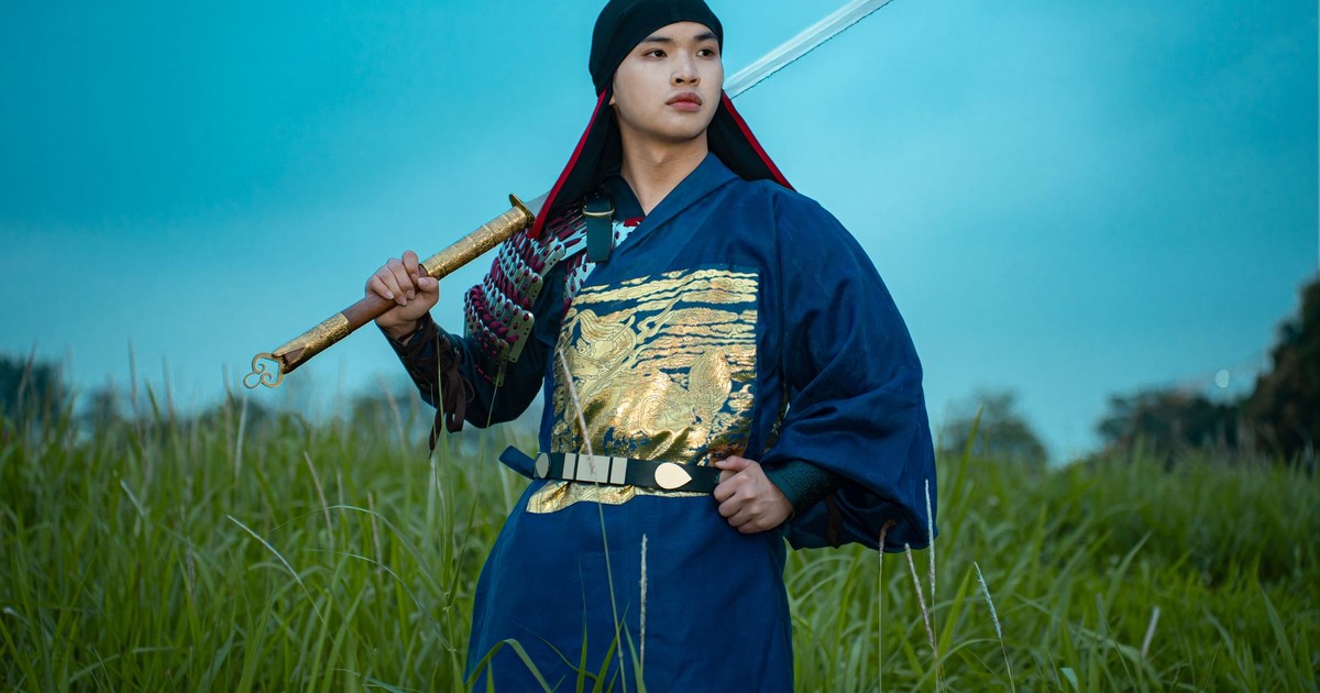 A samurai in traditional attire holds a sword in a grassy field during twilight.