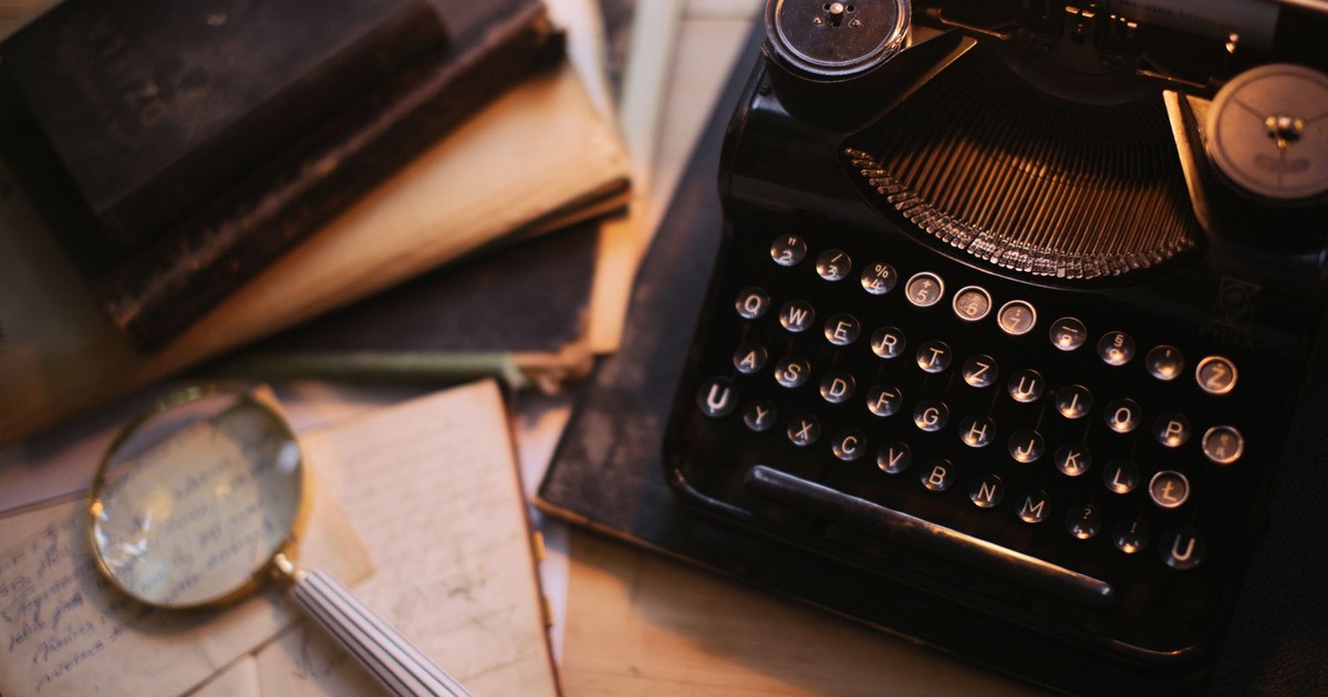 A vintage typewriter with a magnifying glass and old books on a desk, evoking nostalgia.