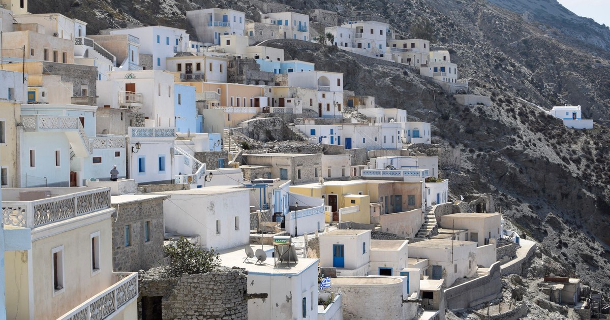 Charming Greek island village with whitewashed houses nestled into a rocky hillside, under a bright sky.