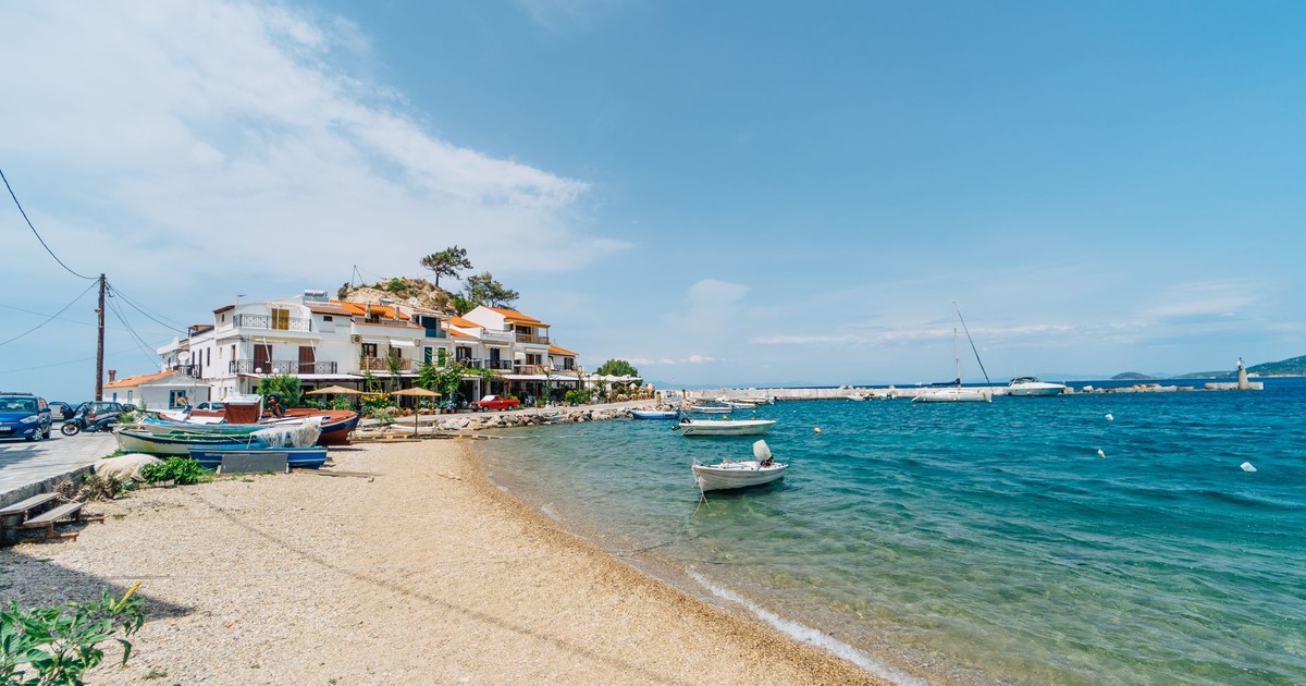 Charming beachfront in Kokkari, Greece with boats and coastal houses under a clear blue sky.