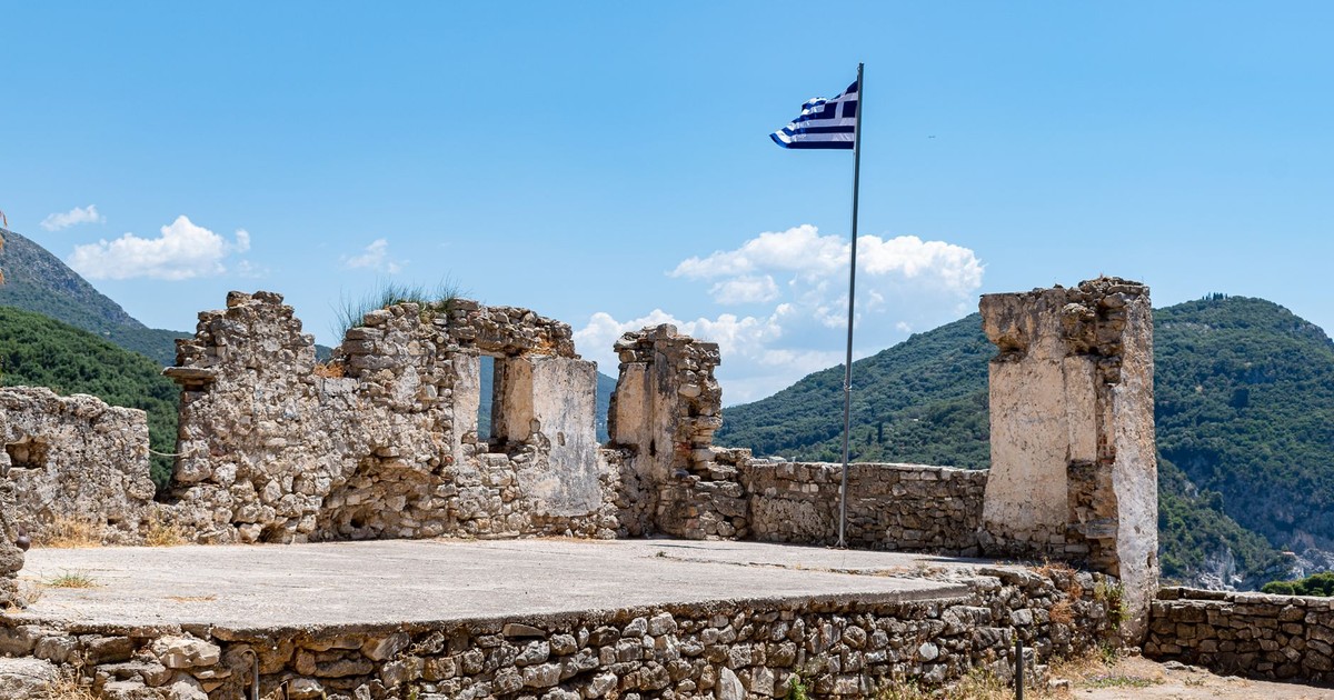 Medieval ruins of Parga Castle overlooking hills with Greek flag. Ideal travel destination.