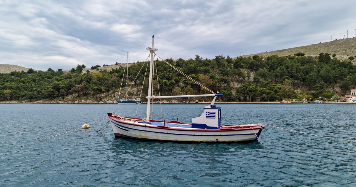 A classic fishing boat anchors peacefully on a calm Greek sea with lush hills in the background.
