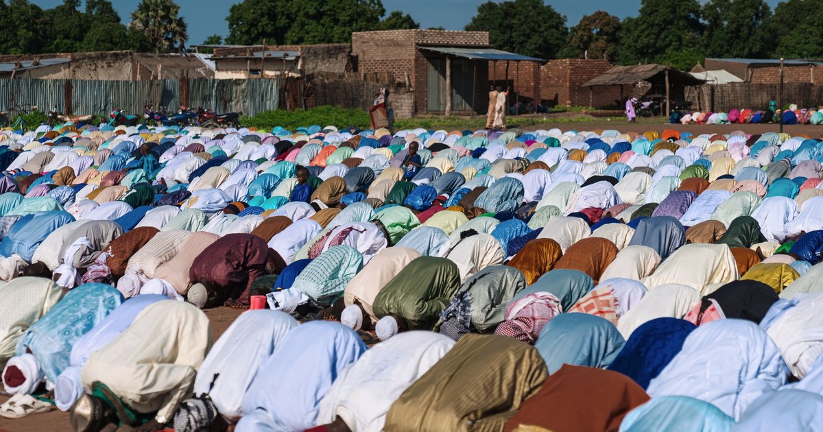 A large group of people are praying outdoors, symbolizing unity and devotion in an open-air setting.