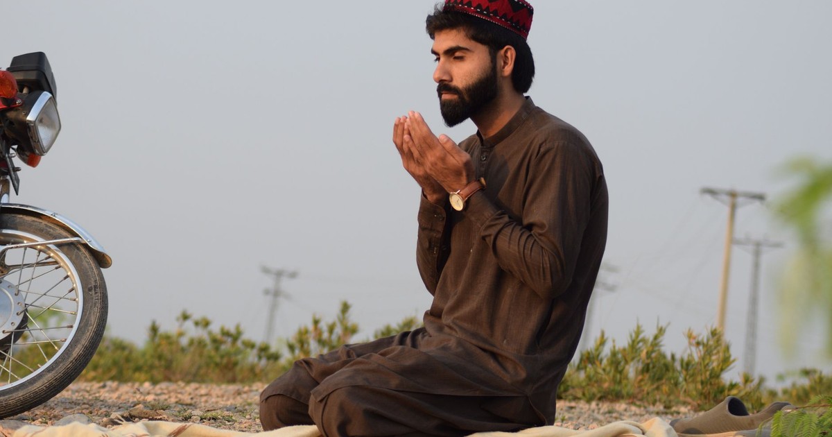A man in traditional attire prays outdoors in Peshawar, Pakistan, showcasing cultural and spiritual themes.