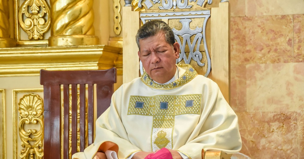 A clergyman dressed in ceremonial robes sits in a beautifully adorned church interior in Baliwag, Philippines.