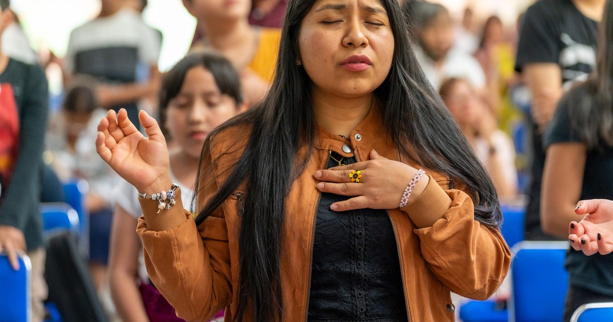 A woman with eyes closed, deeply engaged in prayer during a church service in Mexico City, filled with spirituality.