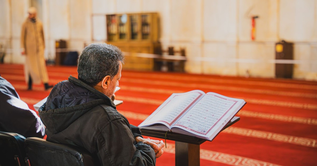 A man sitting in a mosque, attentively reading the Quran. Captures a peaceful moment of reflection.