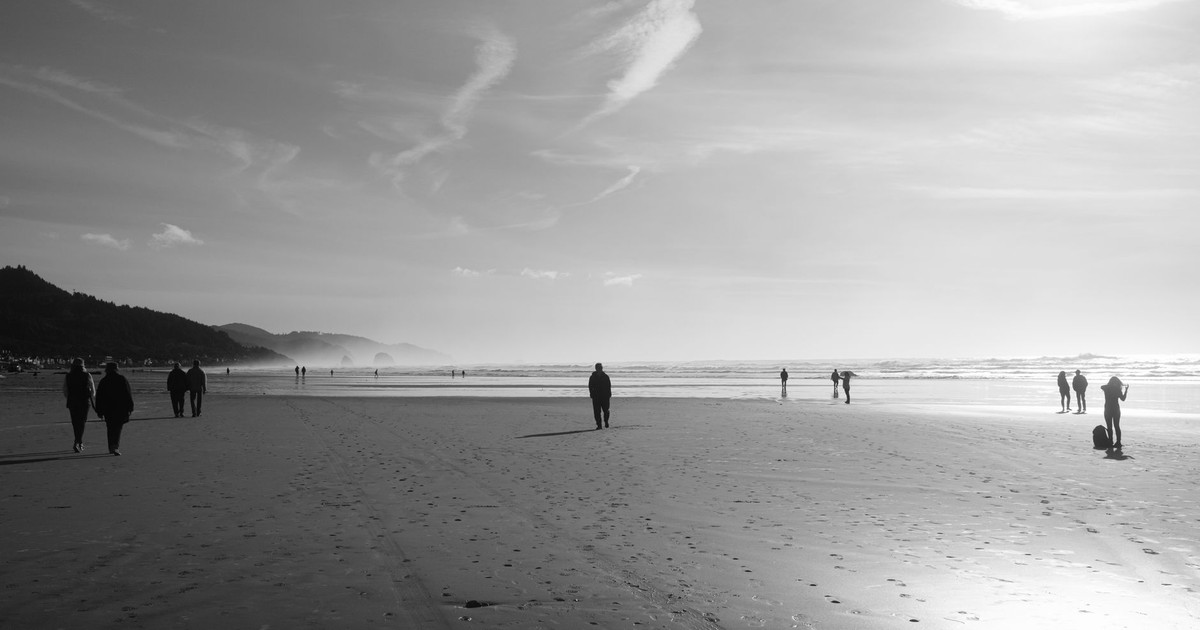 People strolling on Cannon Beach in Oregon, captured in a serene black and white composition.