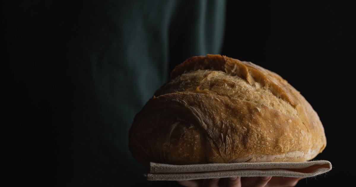 Close-up of a fresh baked loaf of bread held in hands with a dark background.