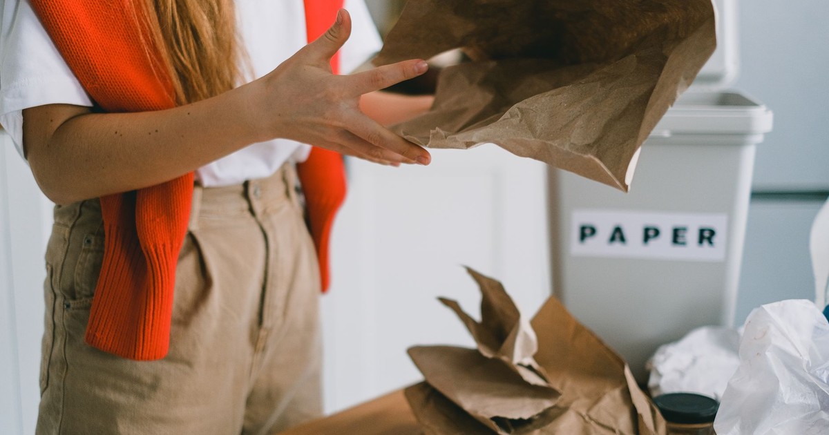 Crop anonymous female standing at table and sorting paper trash from plastic packages and glass