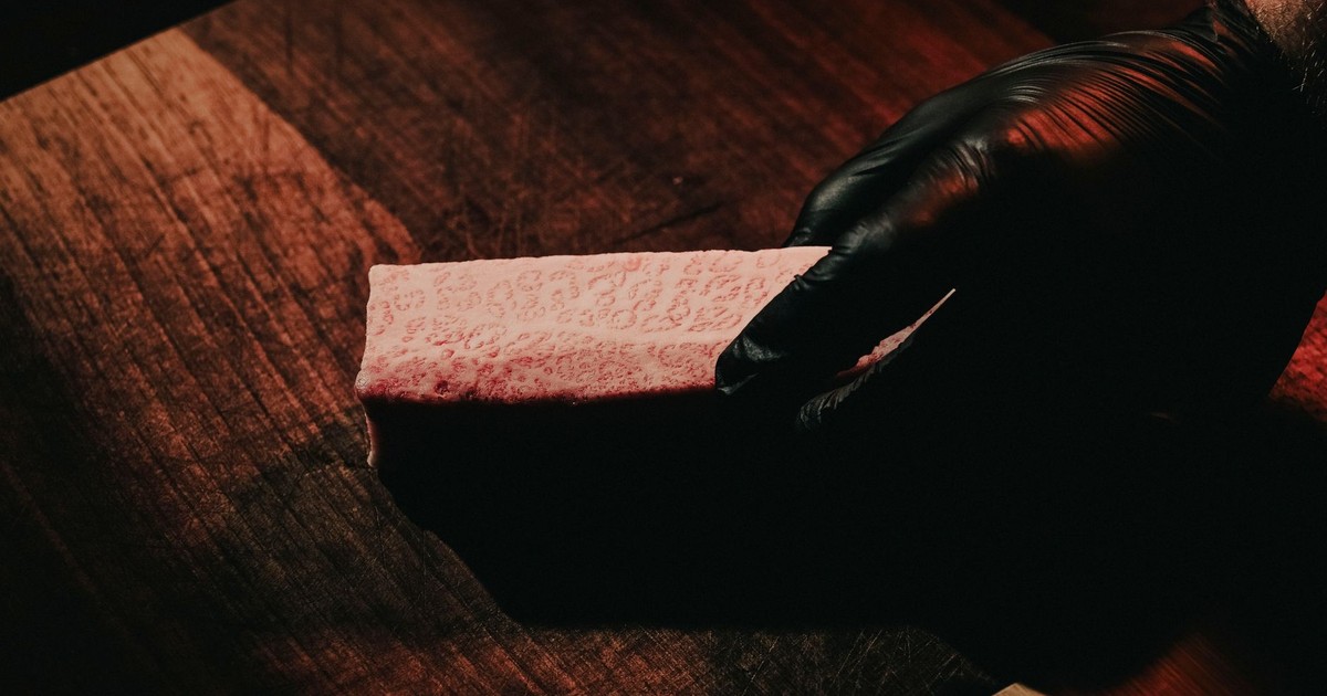 Close-up of a raw Wagyu steak held by a gloved hand on a wooden surface.