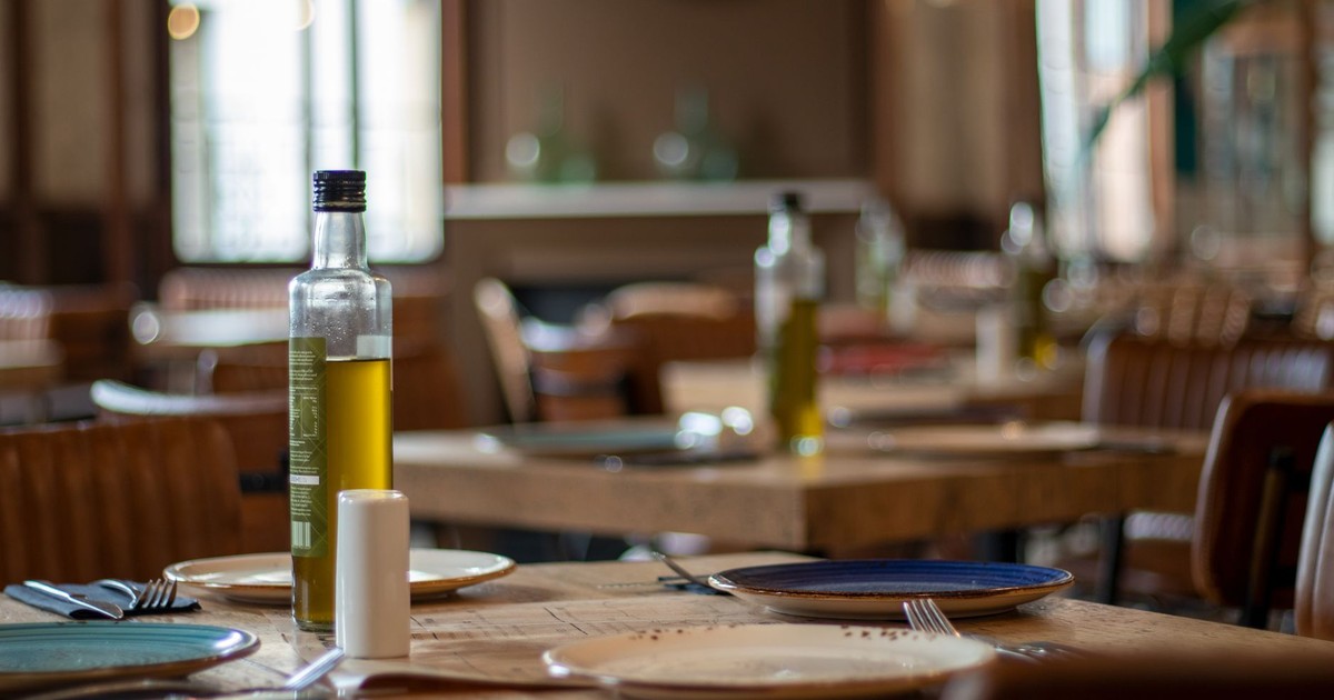 Warm restaurant interior featuring tables set with plates, cutlery, and olive oil.