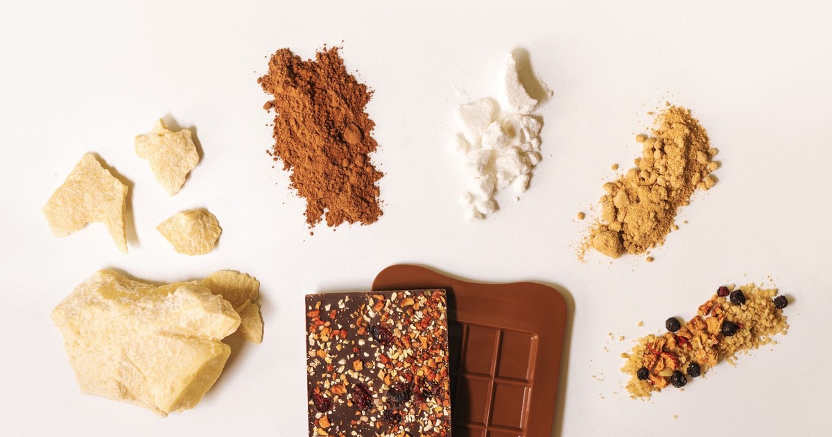 Flat lay of artisan chocolate bar surrounded by raw ingredients on a white background.