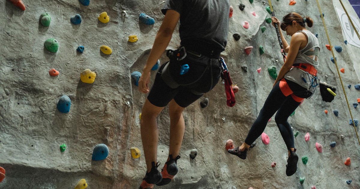 Faceless mountaineers in sportswear hanging on belays during climbing training in modern gym