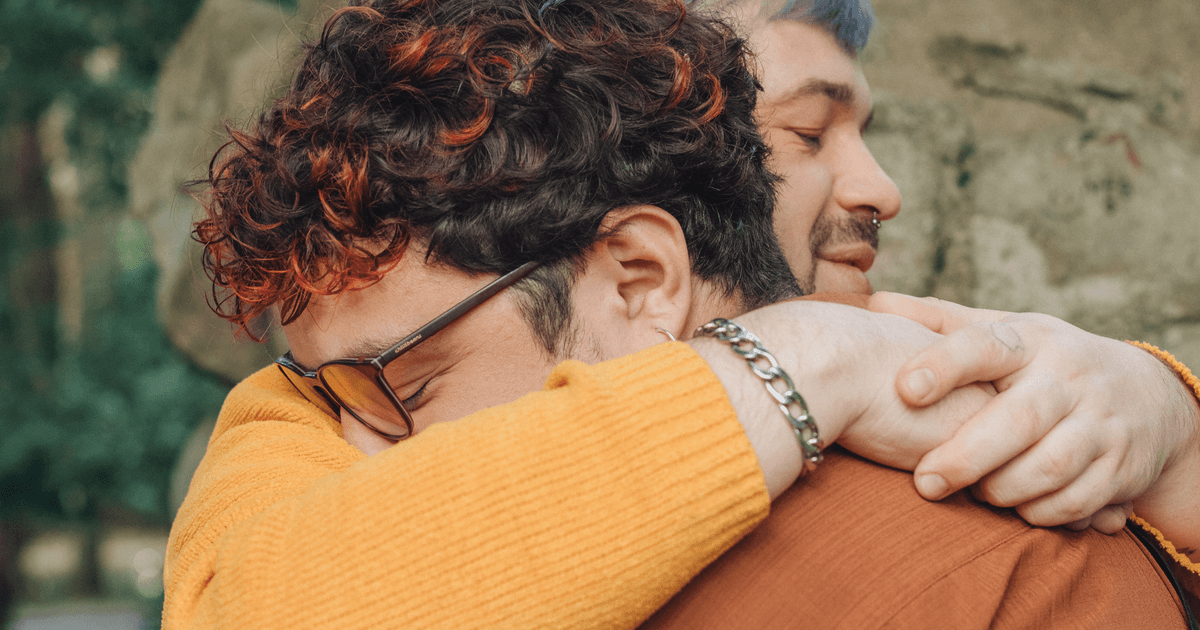 A touching moment of two people embracing outdoors with nature in the background.