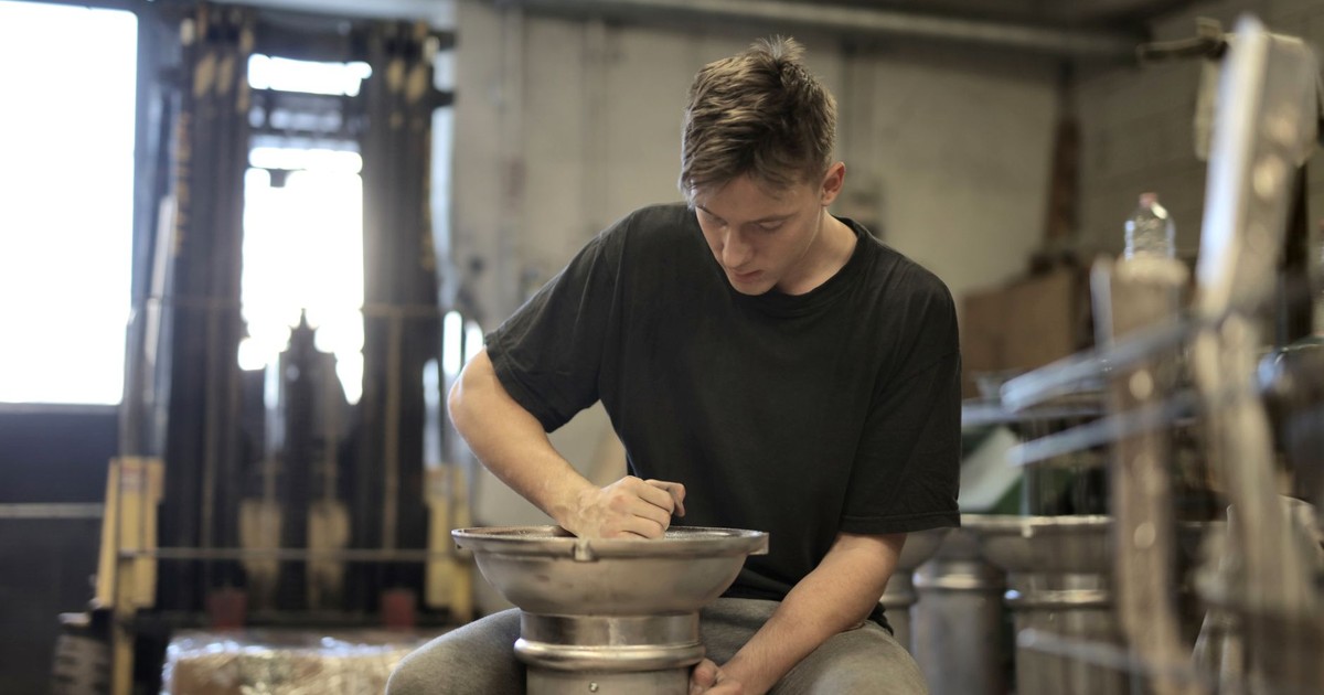 Focused young man working on metal craftsmanship in an industrial workshop setting.