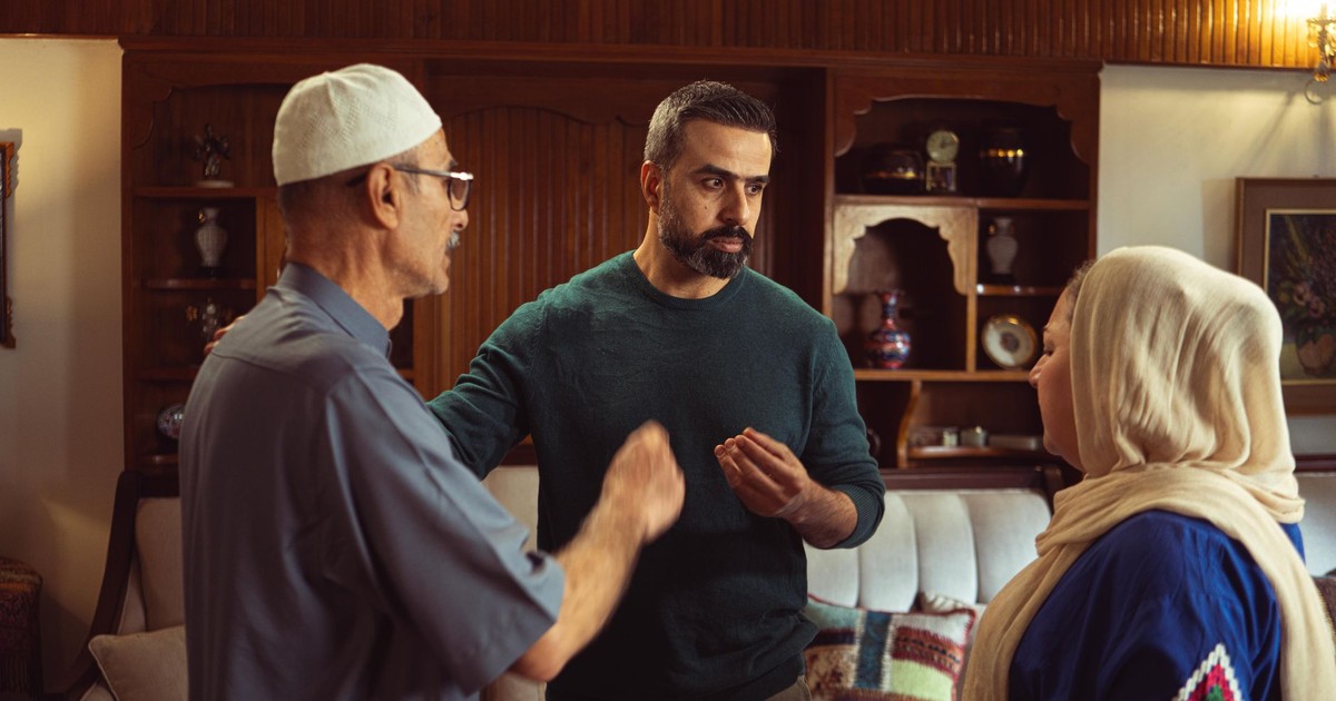 Three adults engaged in a serious conversation indoors, showcasing cultural attire and familial bonds.