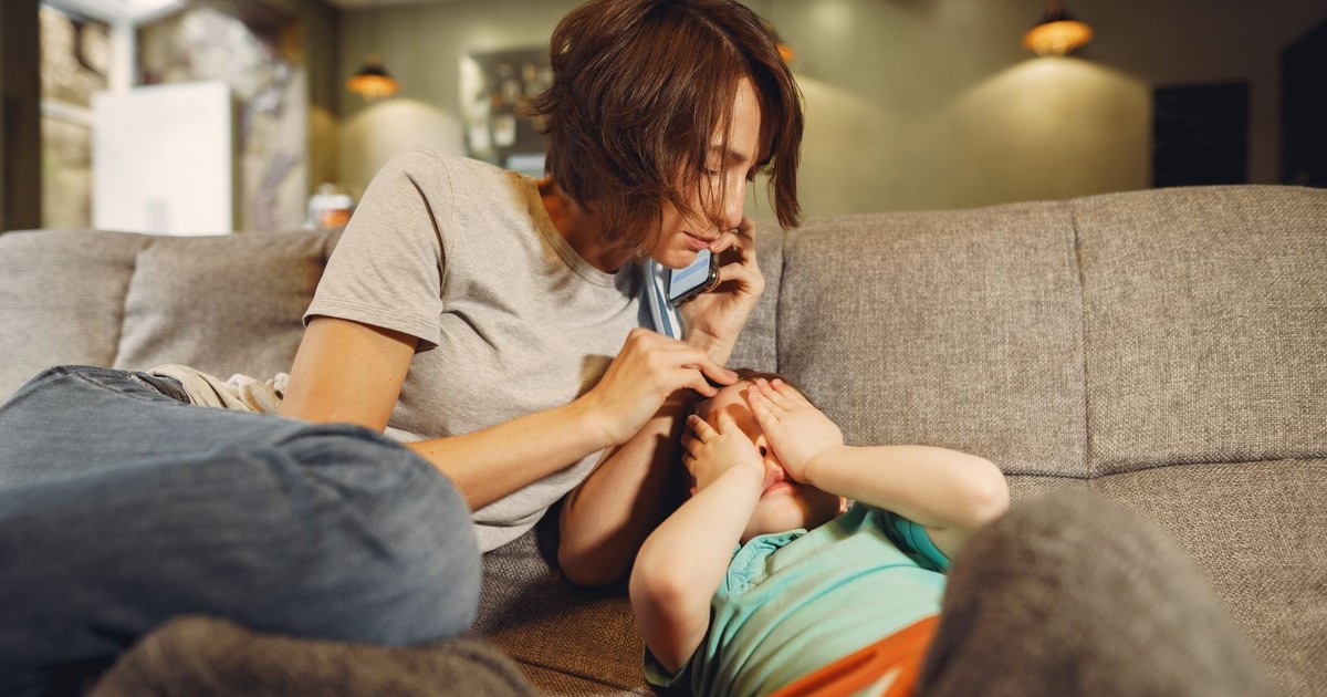 A caring mother on the phone comforts her child on the sofa in a cozy living room.