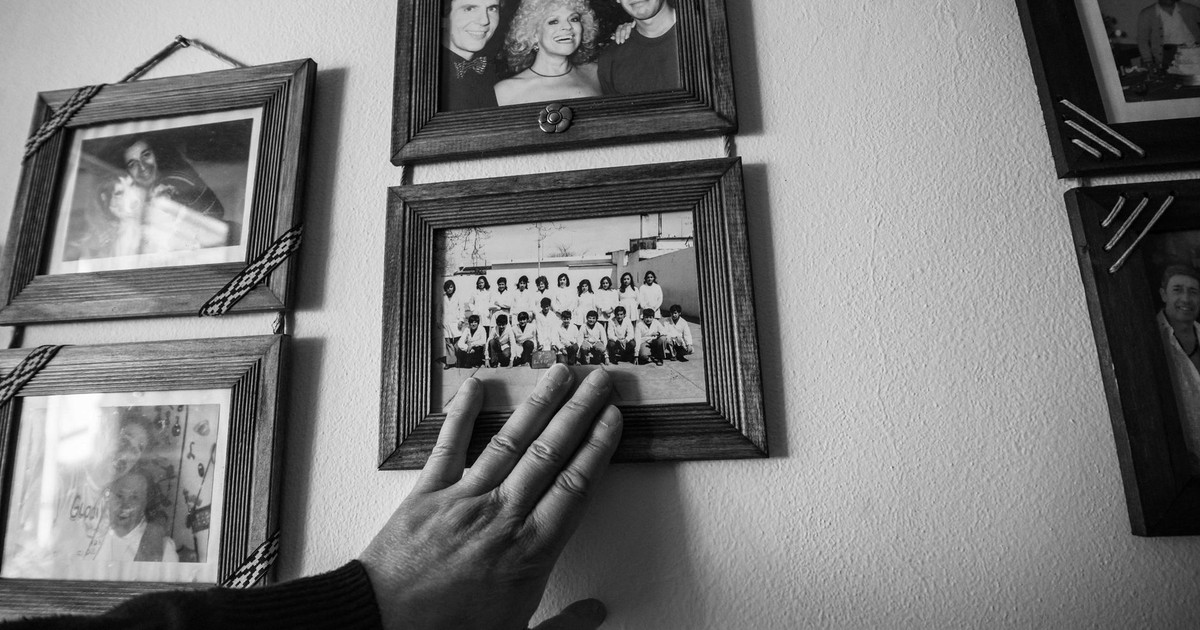 A hand touching vintage black and white framed family photos on a wall, evoking nostalgia.