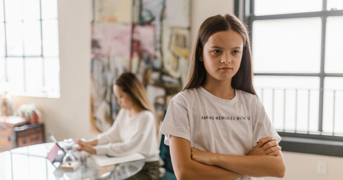 A young girl looks displeased with crossed arms in a modern indoor setting.