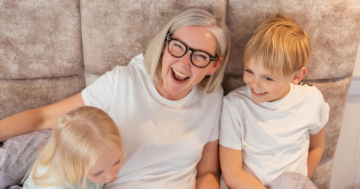 A joyful grandmother with her grandchildren in bed, sharing a happy moment indoors.