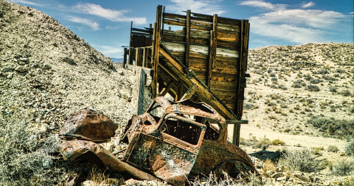 A rusted car wreck near a wooden structure in Nevada's dry, desert landscape.
