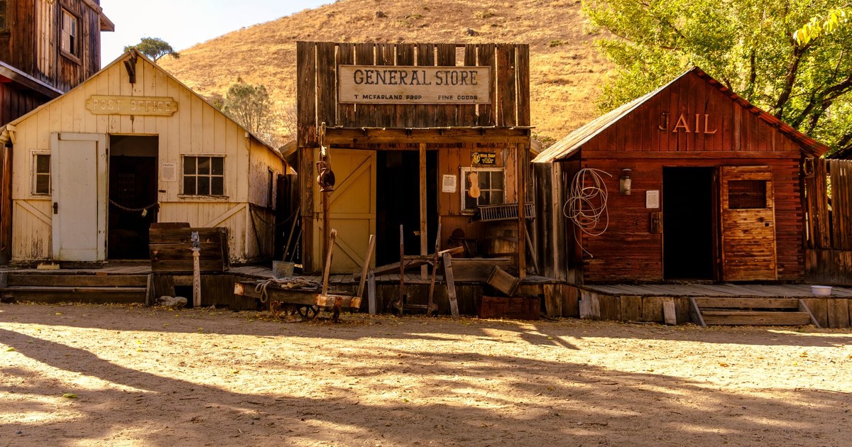 Rustic ghost town with historic general store, old jail, and post office under sunny skies.